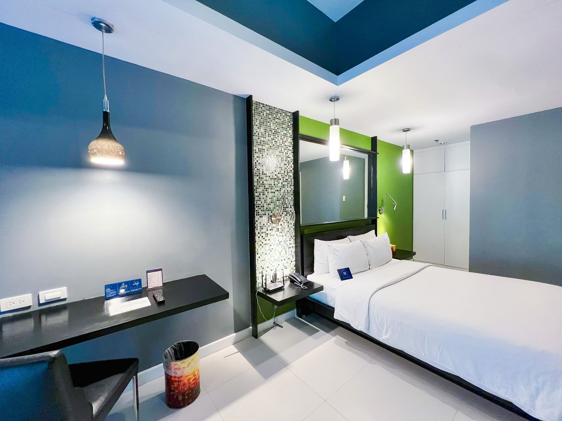 KL Tower hotel bedroom with bed for couples, desk, and modern decor in blue, gray, and green.