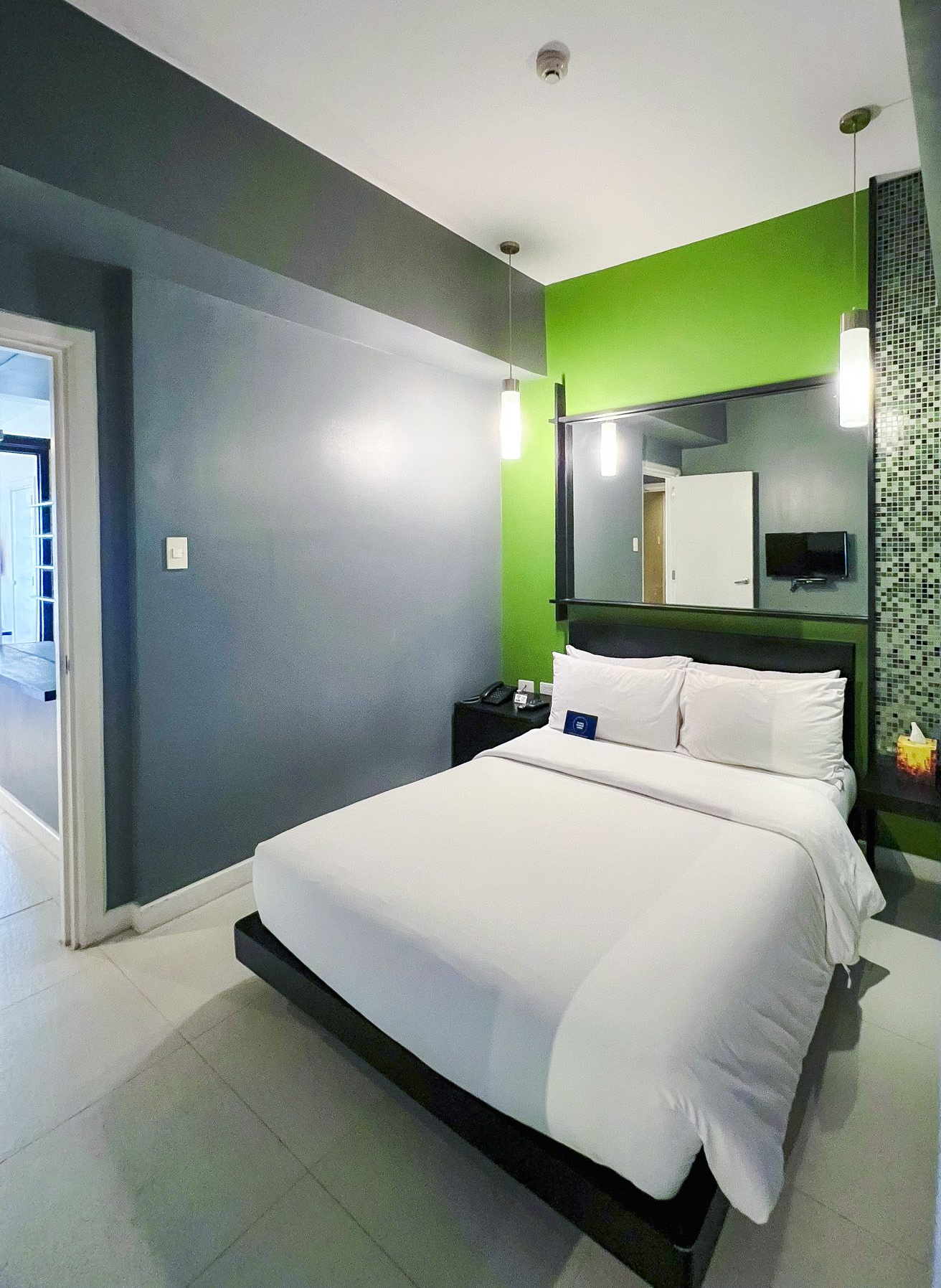 Modern hotel room with green accent wall and comfortable bed, perfect for a relaxing staycation near Greenbelt.