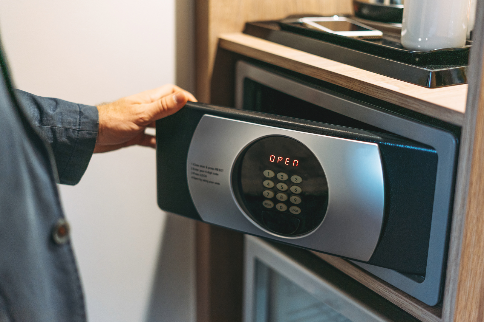 Person opening a digital safe in a hotel room, with a keypad and display visible.
