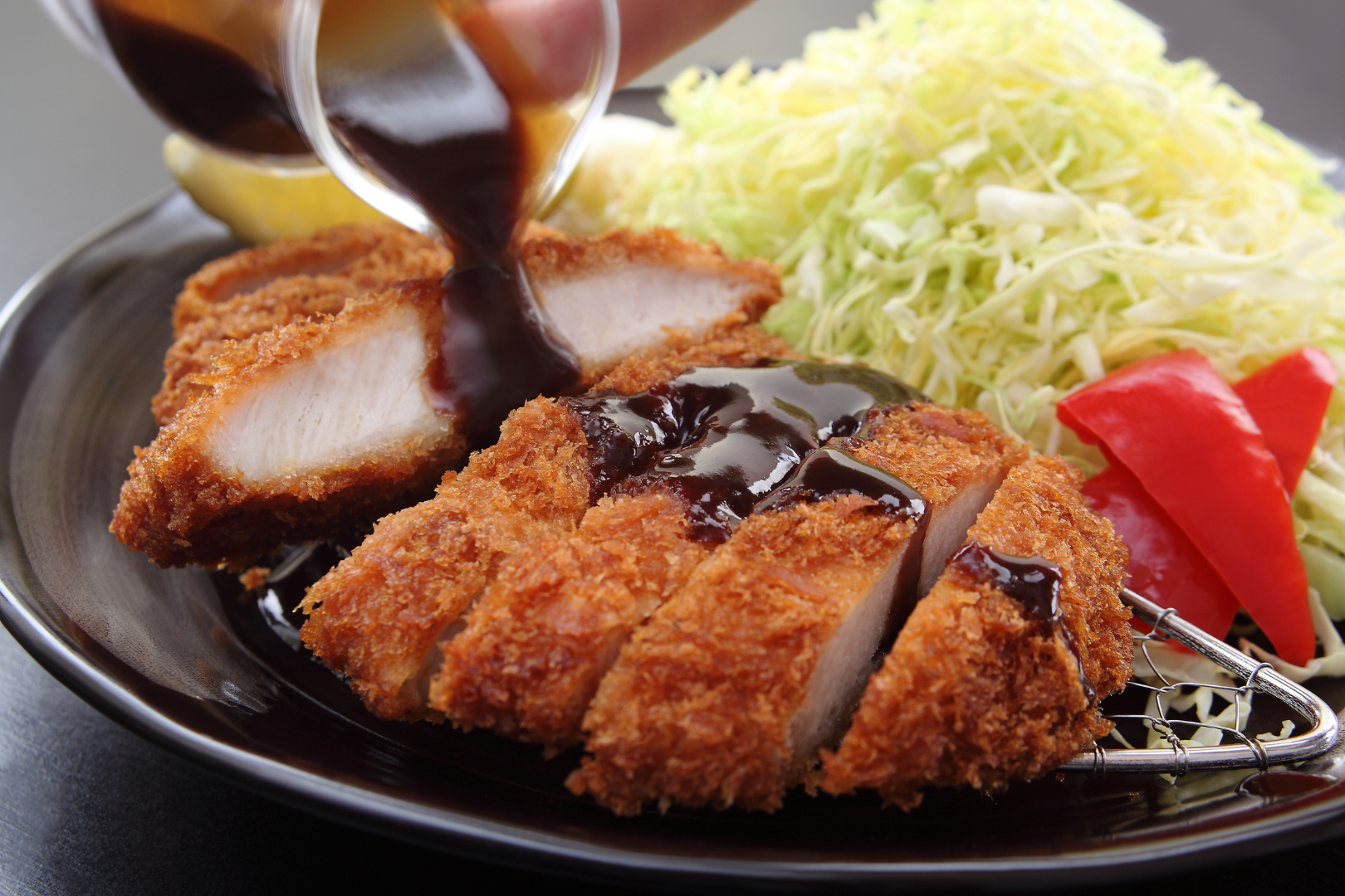 Breaded pork cutlets with sauce, shredded cabbage, and red peppers.