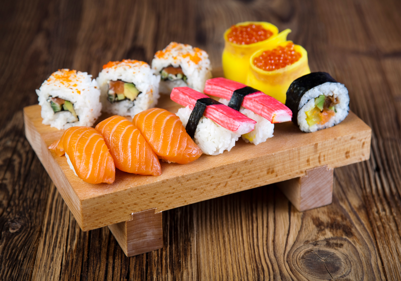 Sushi platter: salmon nigiri, rolls, crab sushi, and fish roe atop a wooden serving board.