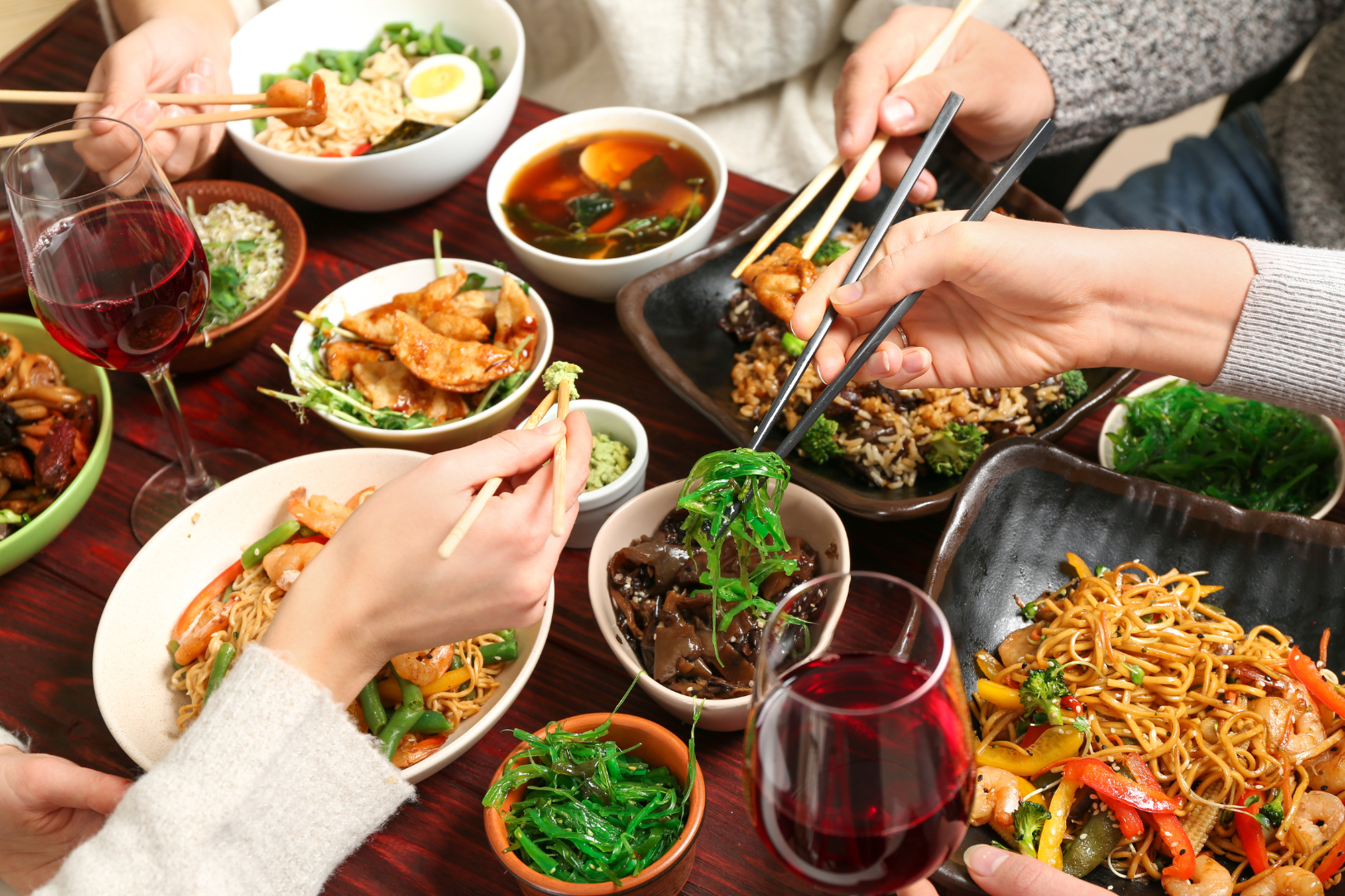 People eating Asian food with chopsticks at a table, various dishes and drinks.