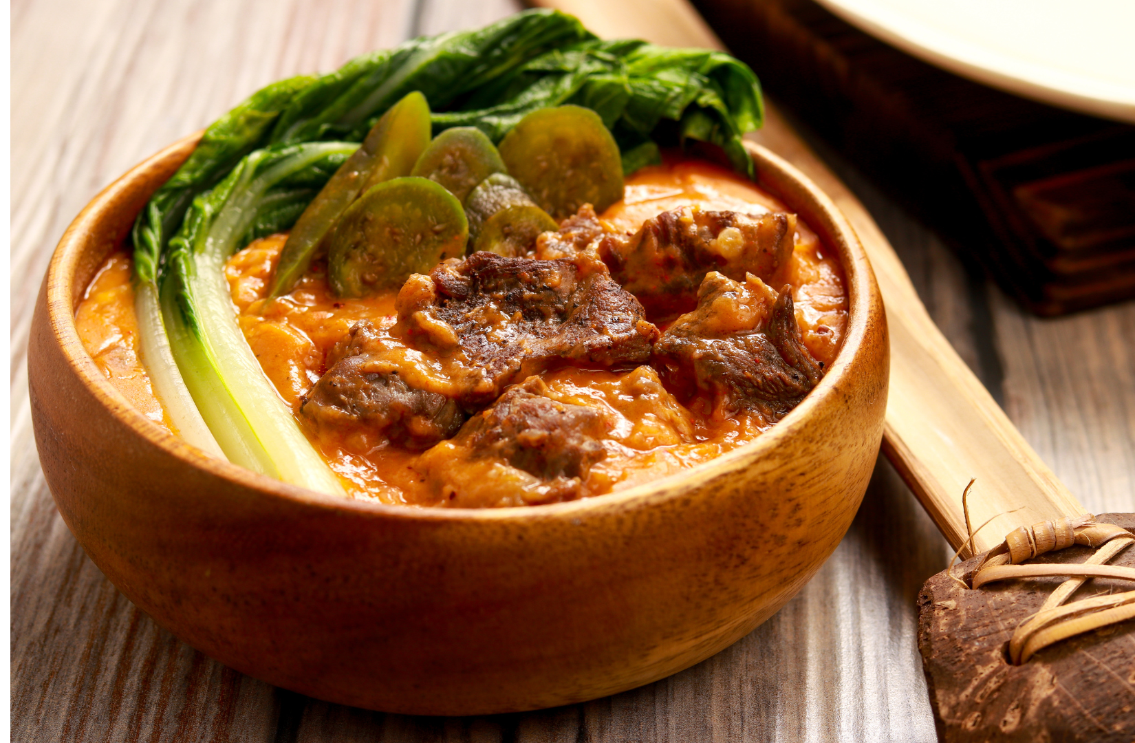Beef kare-kare in a wooden bowl, topped with vegetables.