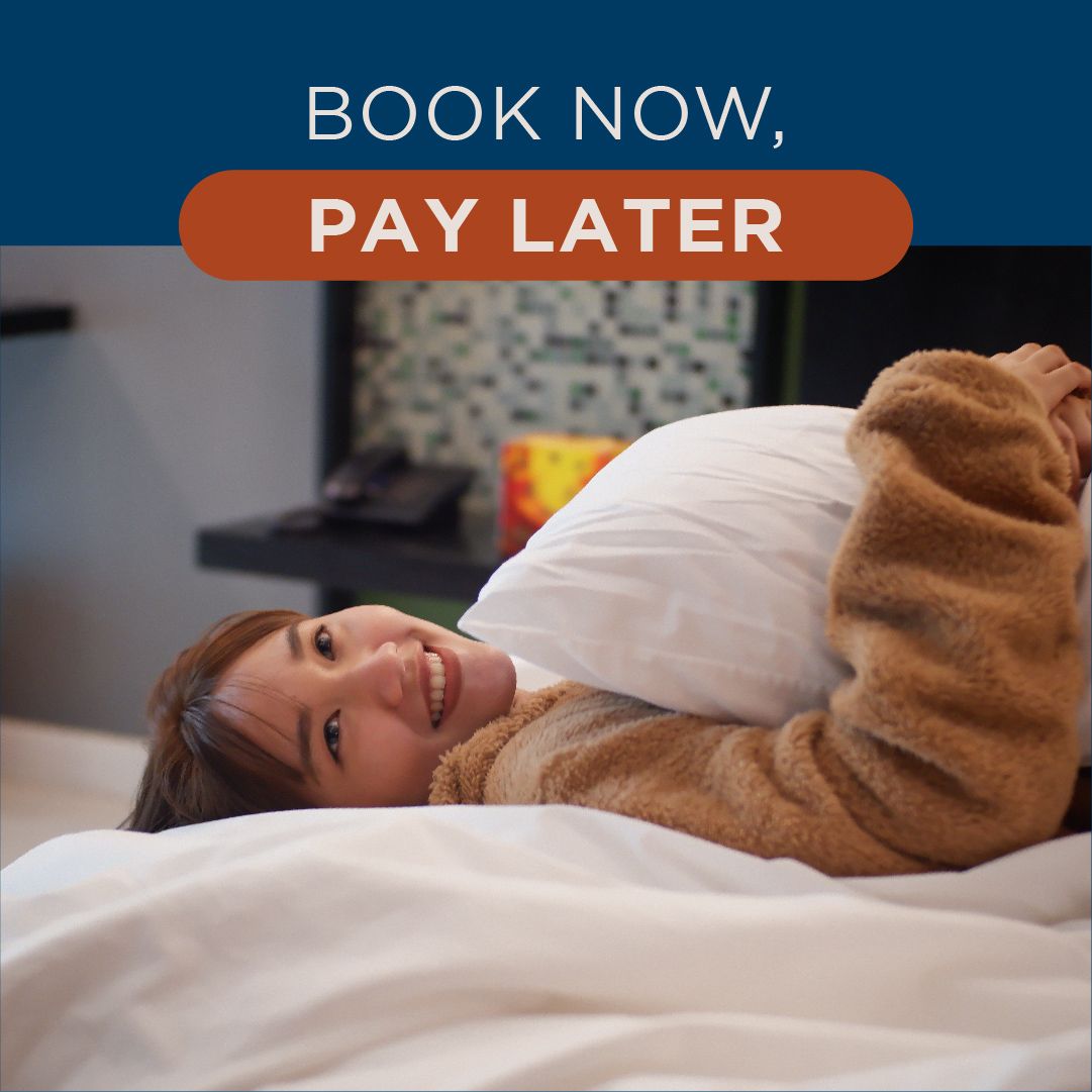 A woman is laying on a bed with a book now pay later sign above her