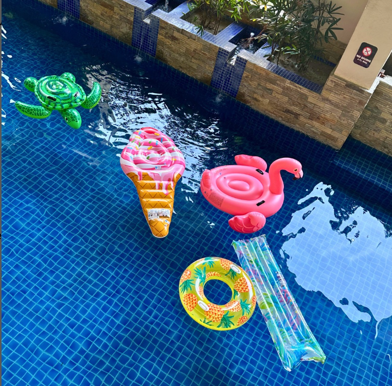 Pool with floating inflatable toys: ice cream, flamingo, turtle, pineapple ring, and raft.