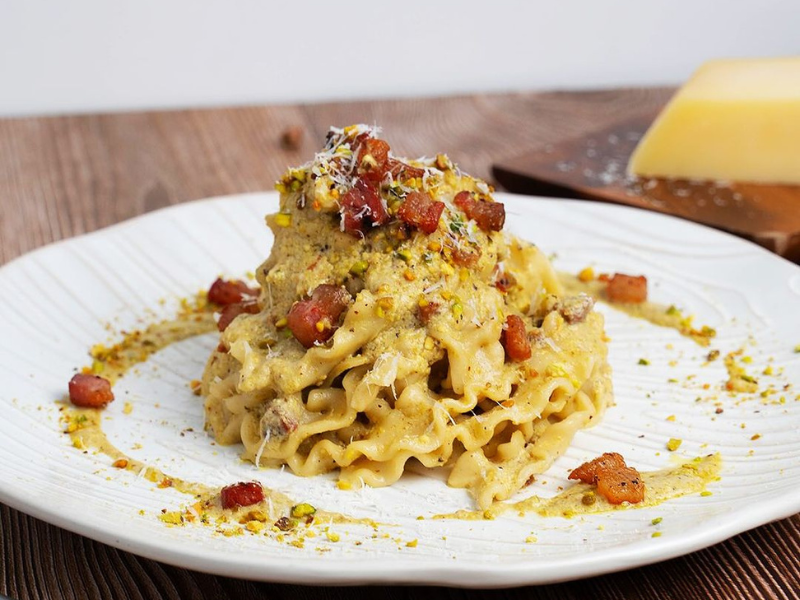 Pasta dish with bacon, pistachios, and parmesan on a white plate.