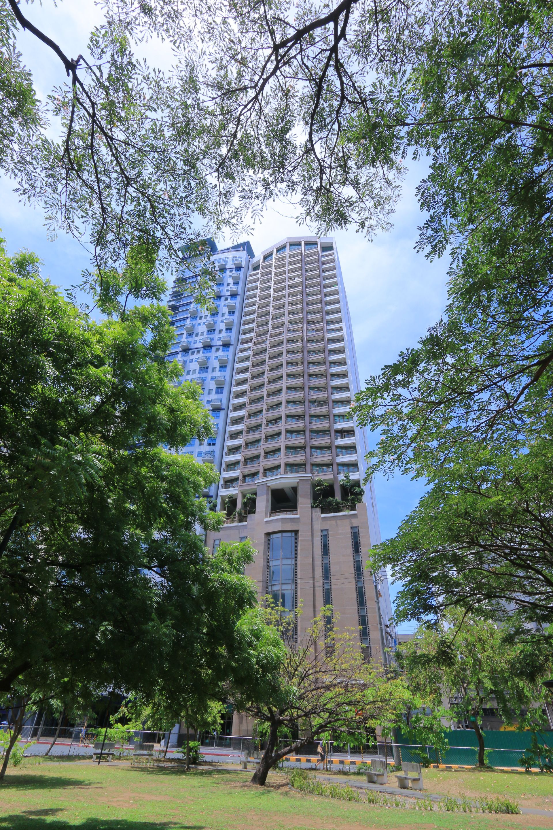 Exterior of KL Tower Serviced Residences in Makati, a high-rise framed by leafy trees in a neighboring park
