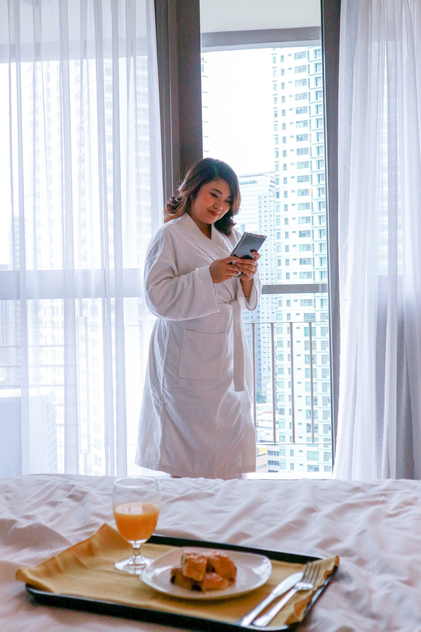 Woman in bathrobe enjoying morning views and refreshments during her hotel stay near Greenbelt