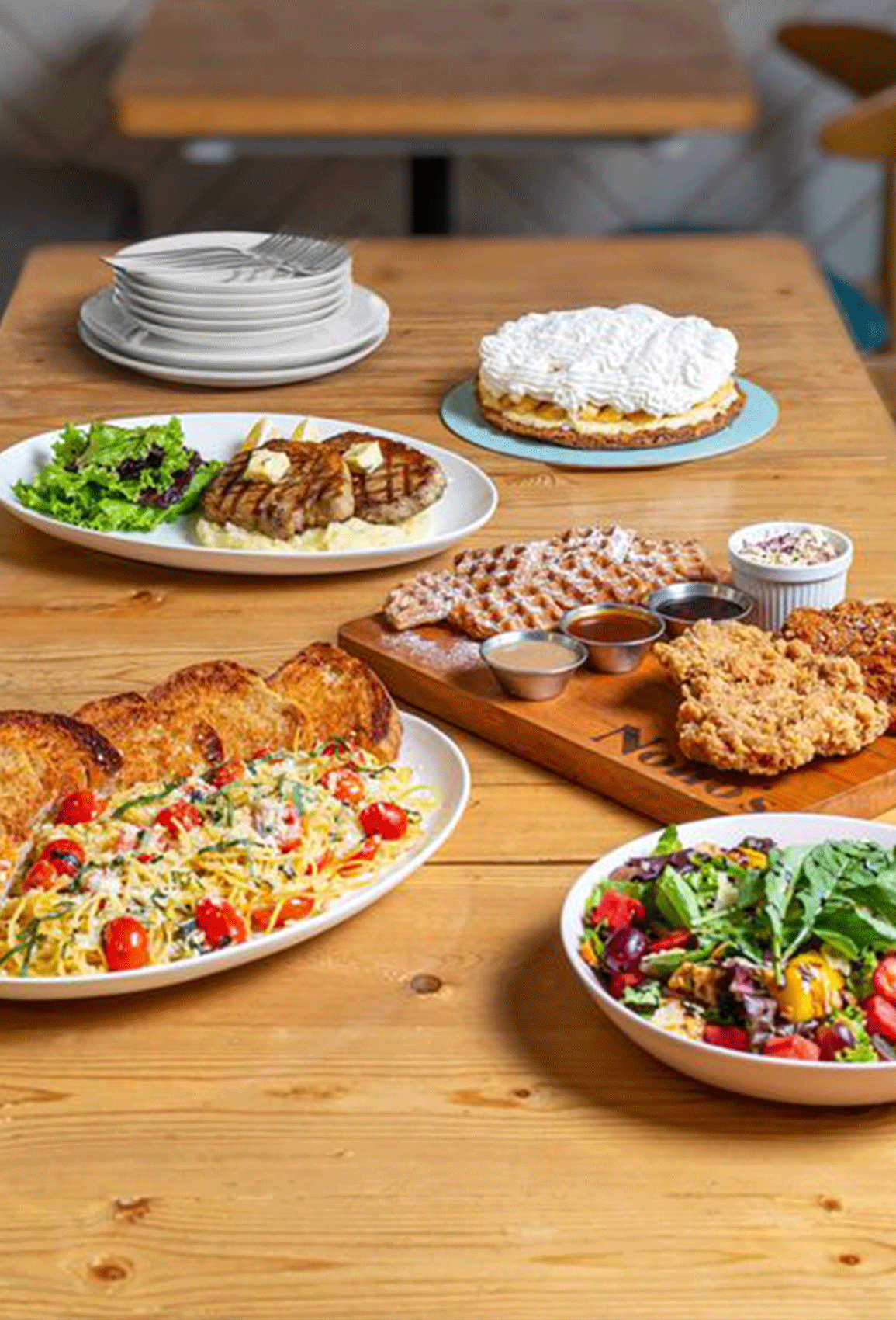Assorted dishes on a wooden table, including pasta, salad, breaded chicken, dessert, and soup.