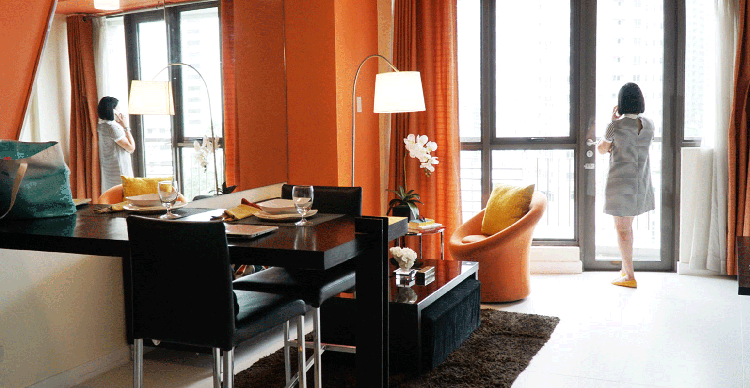 Modern apartment dining area with orange walls and a person standing by a bright window.