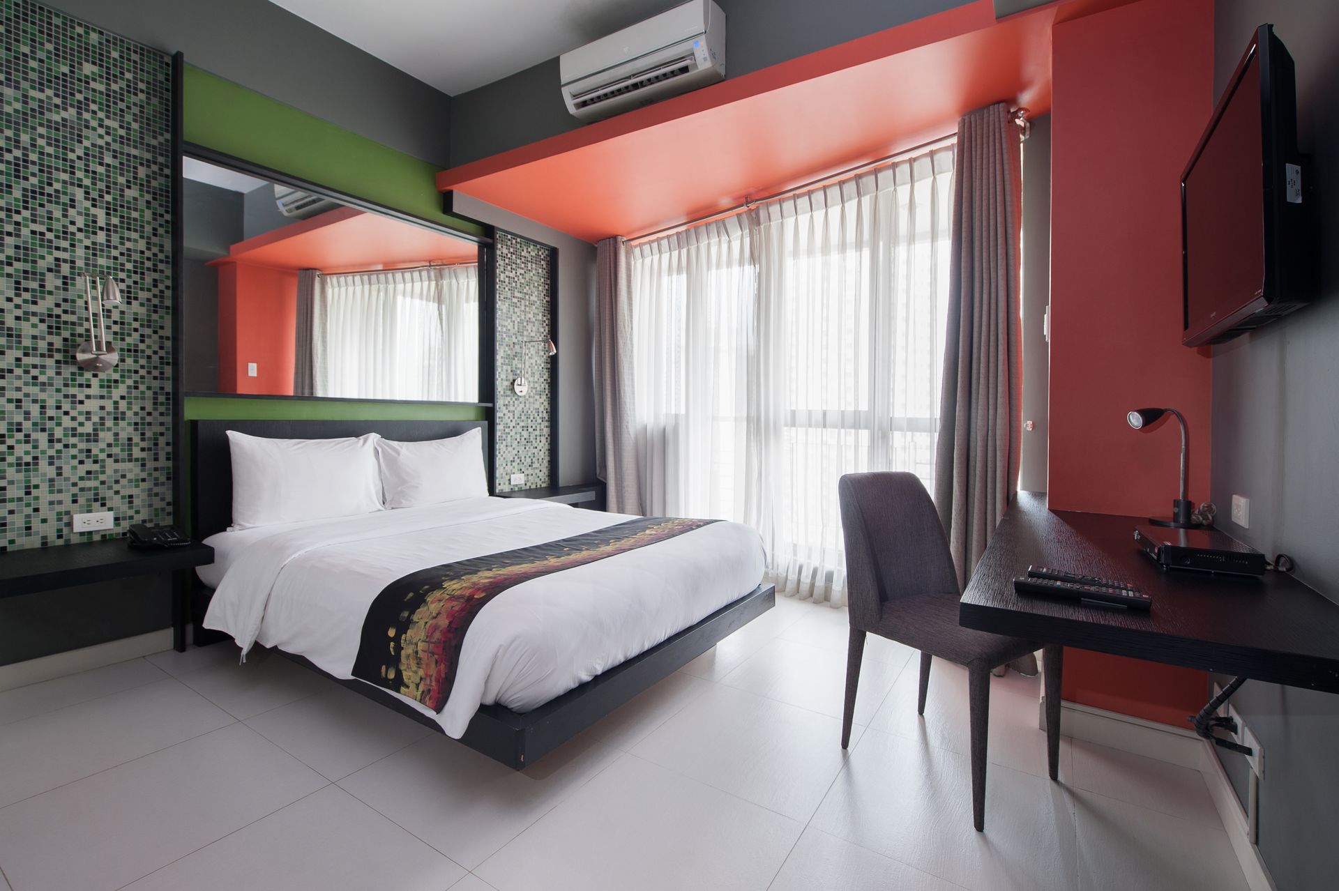 Bedroom at KL Tower Makati with a double bed, mosaic-tiled wall, red and green accents, and a work desk by the TV