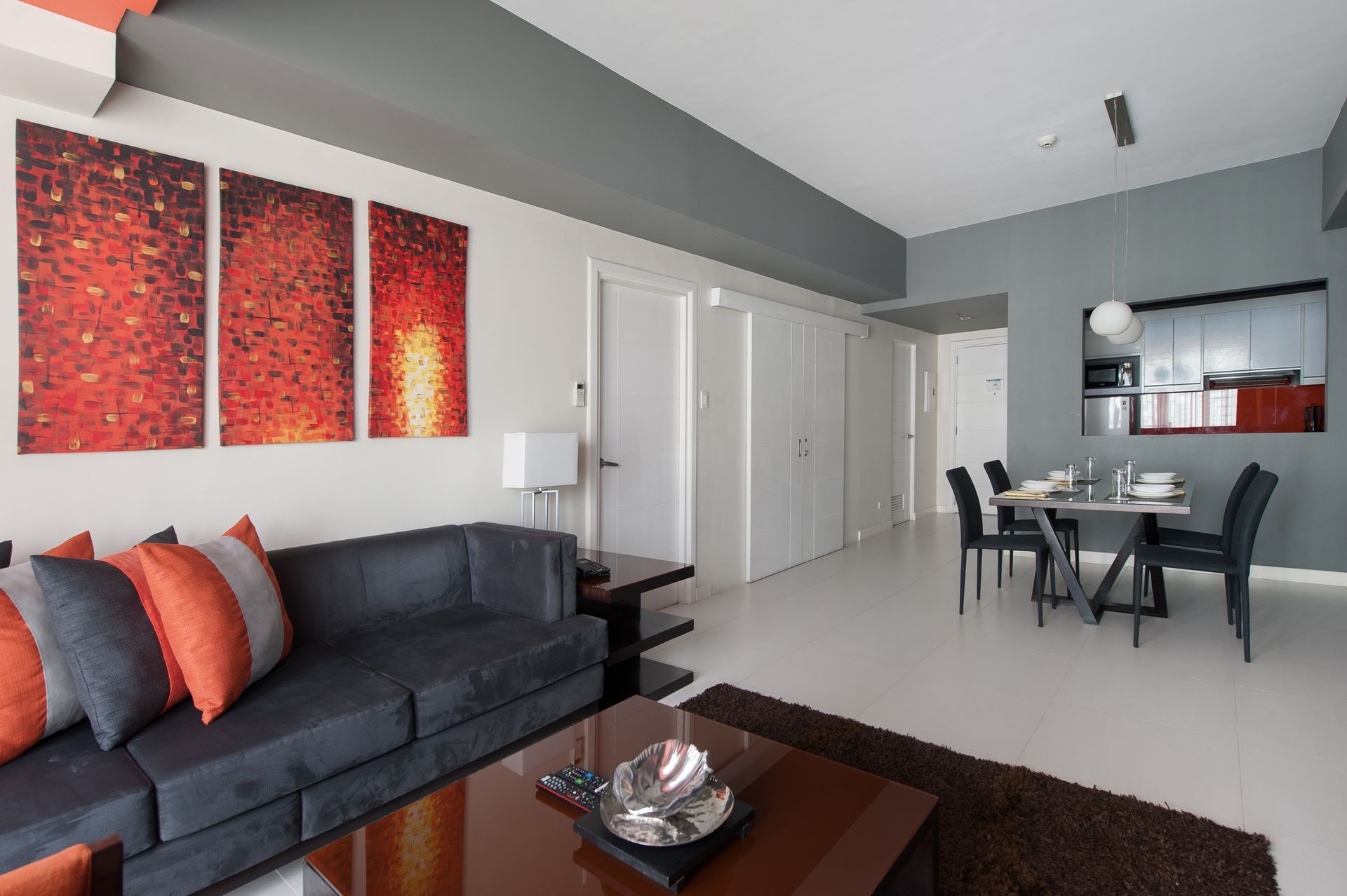 Living and dining area of the One Bedroom Executive at KL Tower Makati with a gray sofa, orange accents, and triptych art
