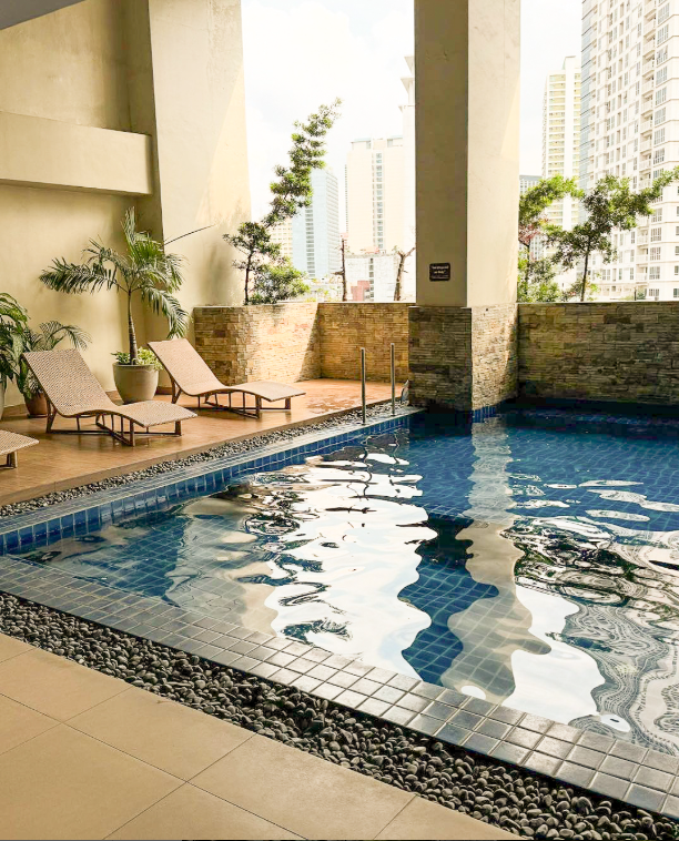 A swimming pool on a terrace with lounge chairs and tall buildings in the background.