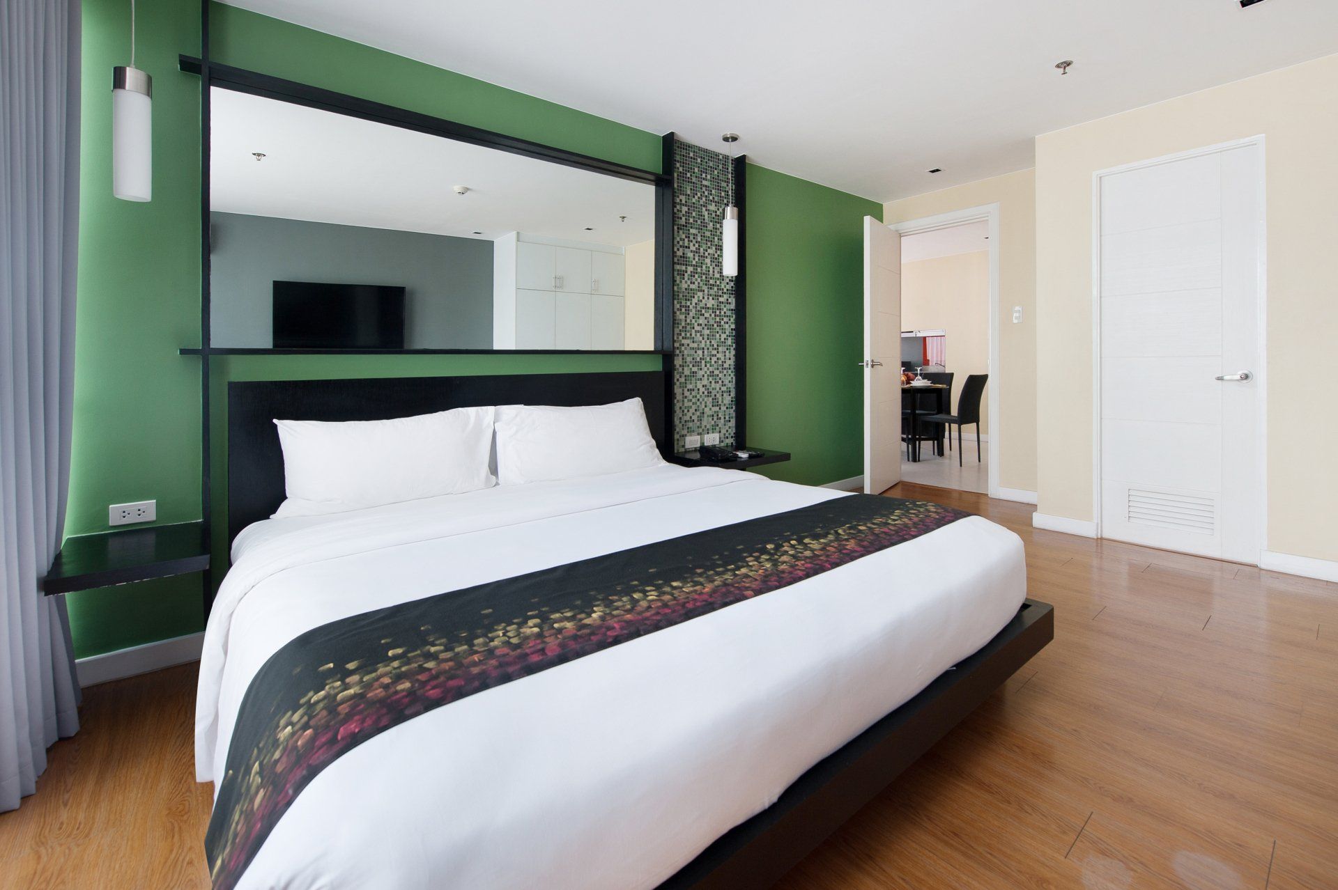 Modern bedroom at KL Serviced Residences with a black-framed bed, green accent wall, large mirror, and wood floor