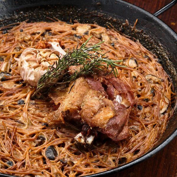Vermicelli dish with roasted meat, garlic, and rosemary sprig in a pan.