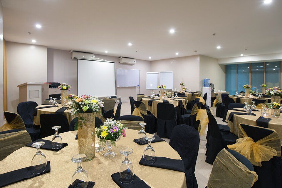 A banquet room arranged with round tables featuring gold tablecloths, black chair covers, and floral centerpieces.