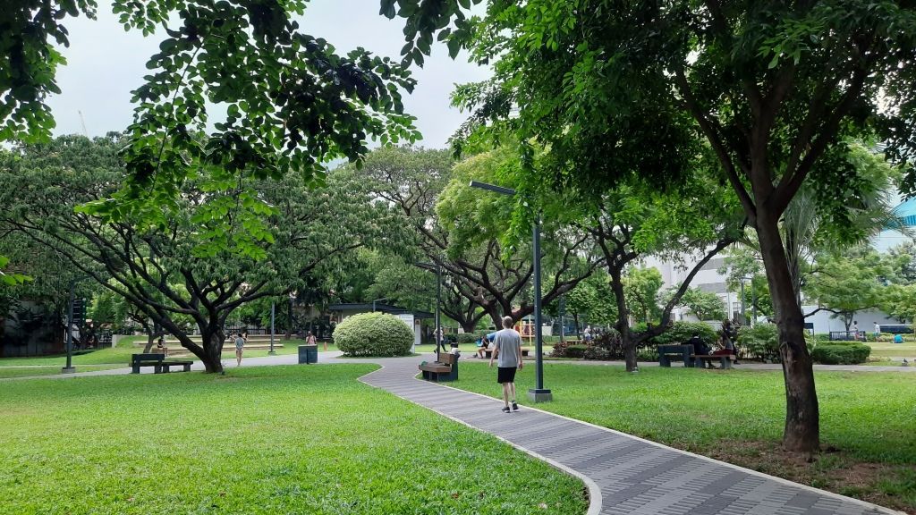 Curved park path through green trees and grass, with a few people walking in the distance.