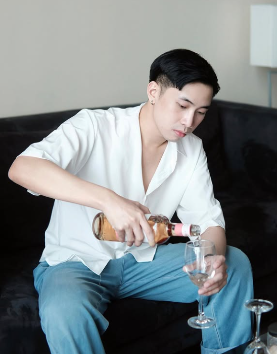 Young man pouring a drink while relaxing on a dark sofa in a hotel room.
