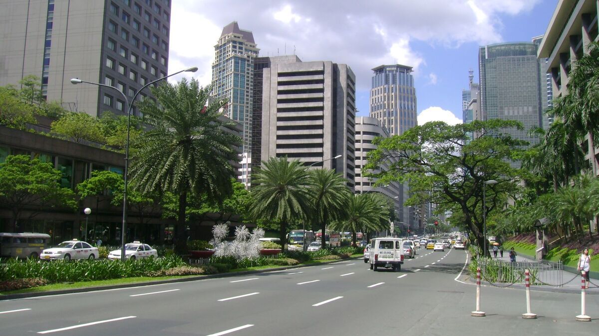 A wide road with buildings and palm trees in a city setting under a blue sky.