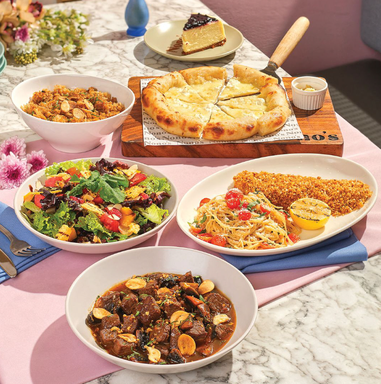 Assorted plated dishes on a table, including pizza, salad, pasta, stew, and dessert in a cozy dining setting