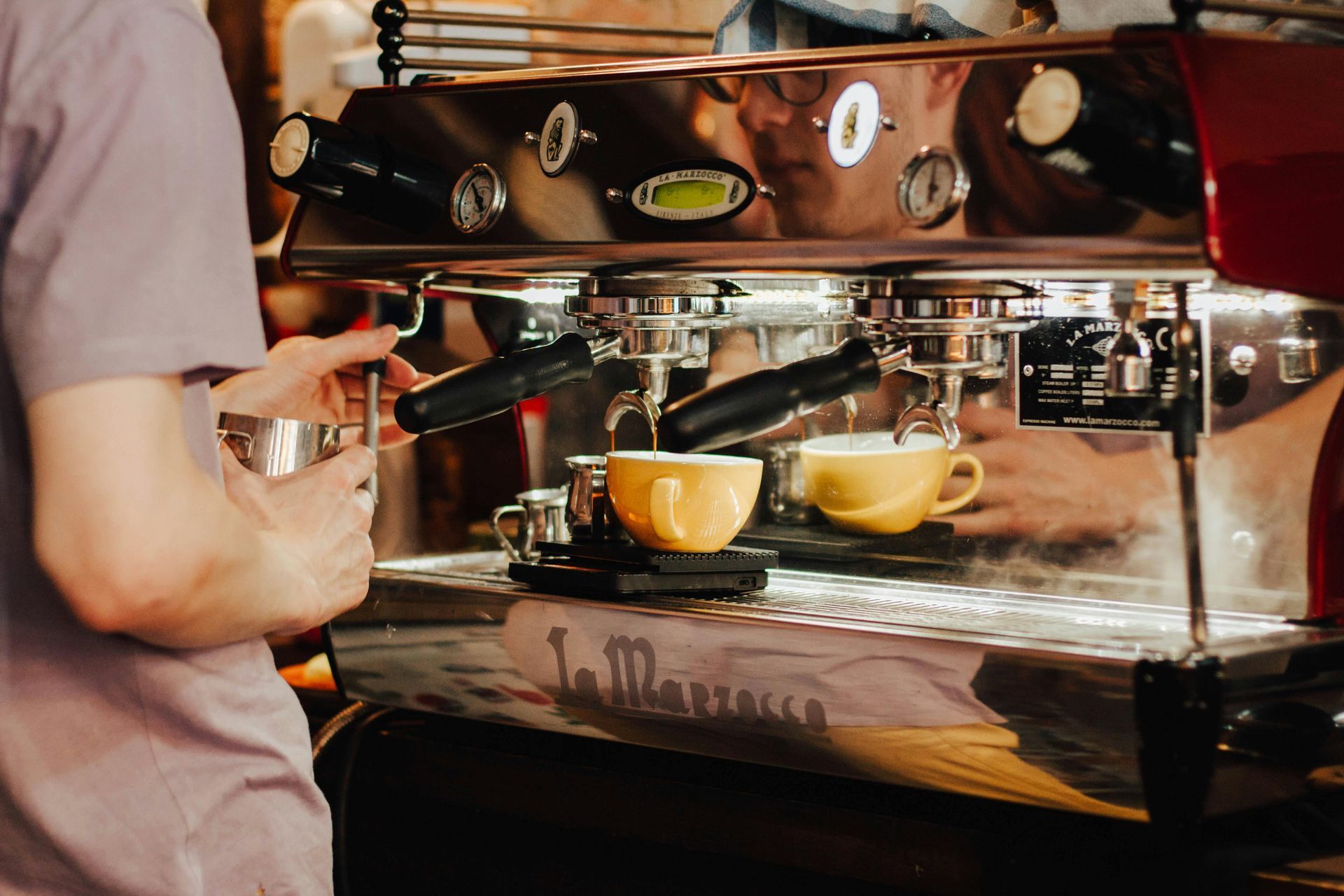 Barista using espresso machine to make coffee; two yellow cups are filling.