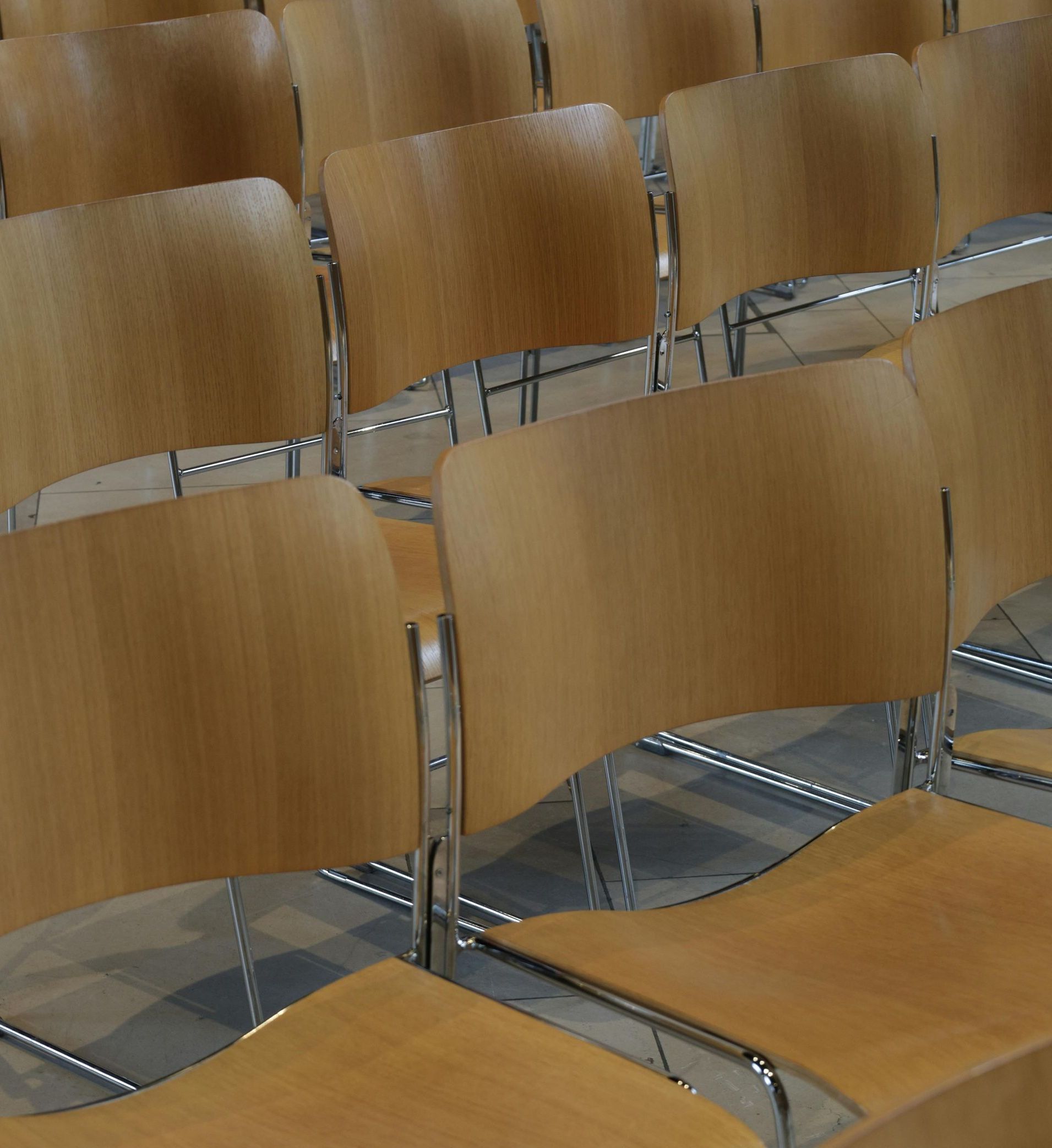 Rows of empty wooden chairs with chrome legs in a conference hall