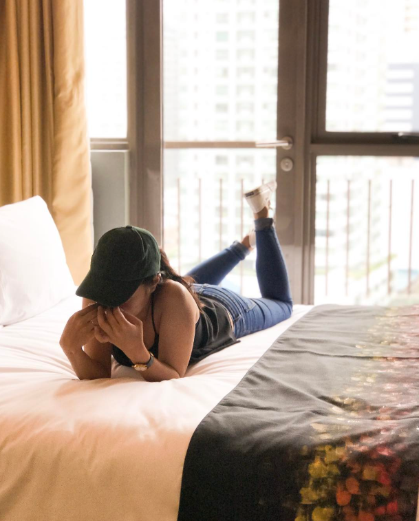 Woman lying on a bed near a window, enjoying a peaceful moment in natural light.