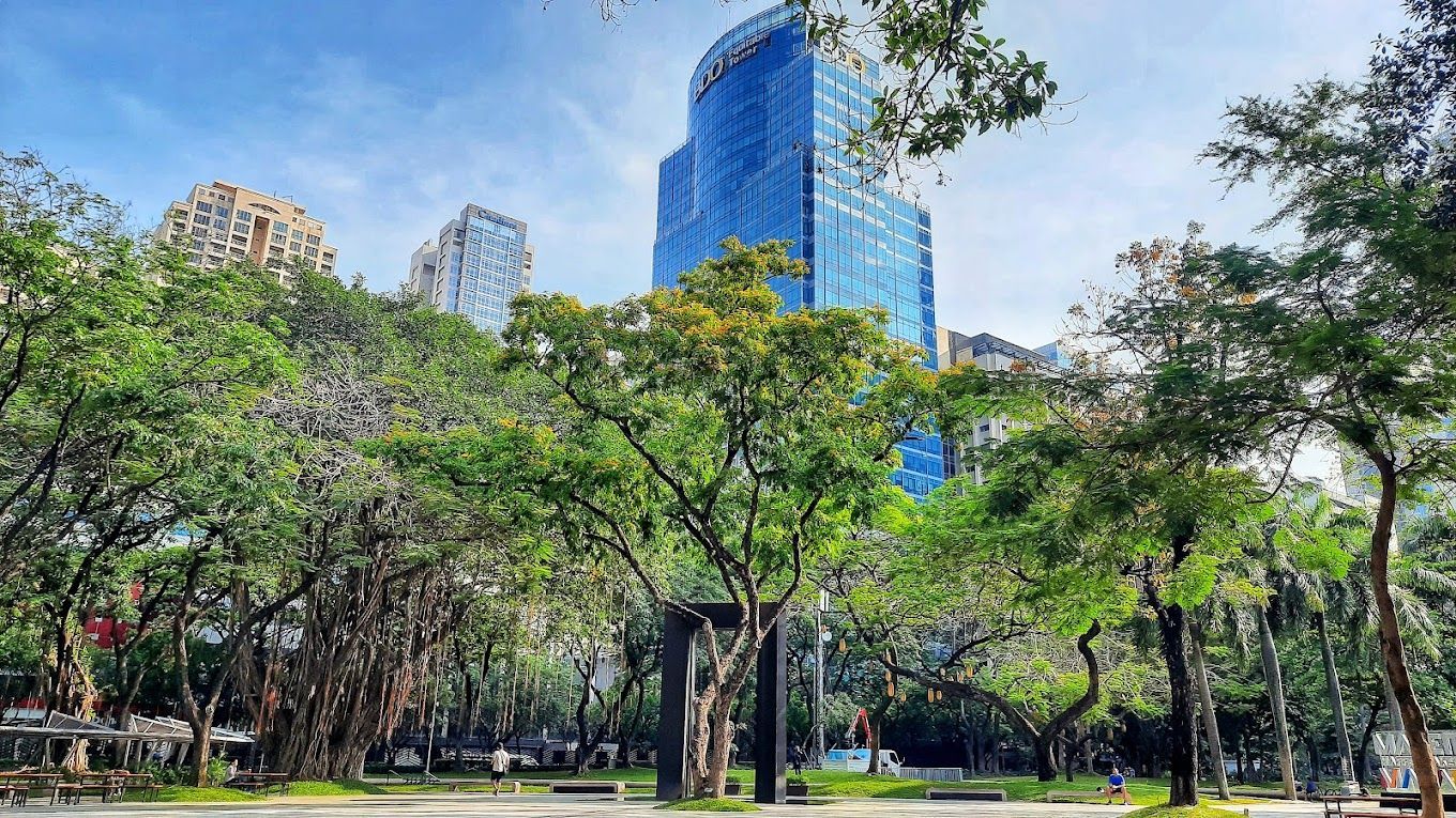 Park with trees and tall blue skyscraper in the background on a sunny day.