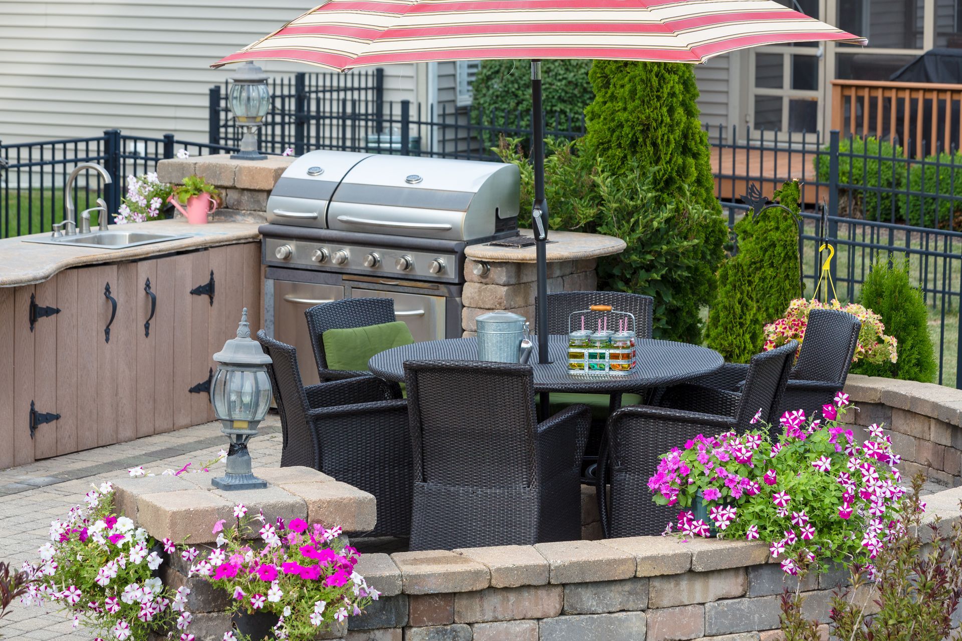 Patio seating area with grill, umbrella, and flowers behind a stone retaining wall