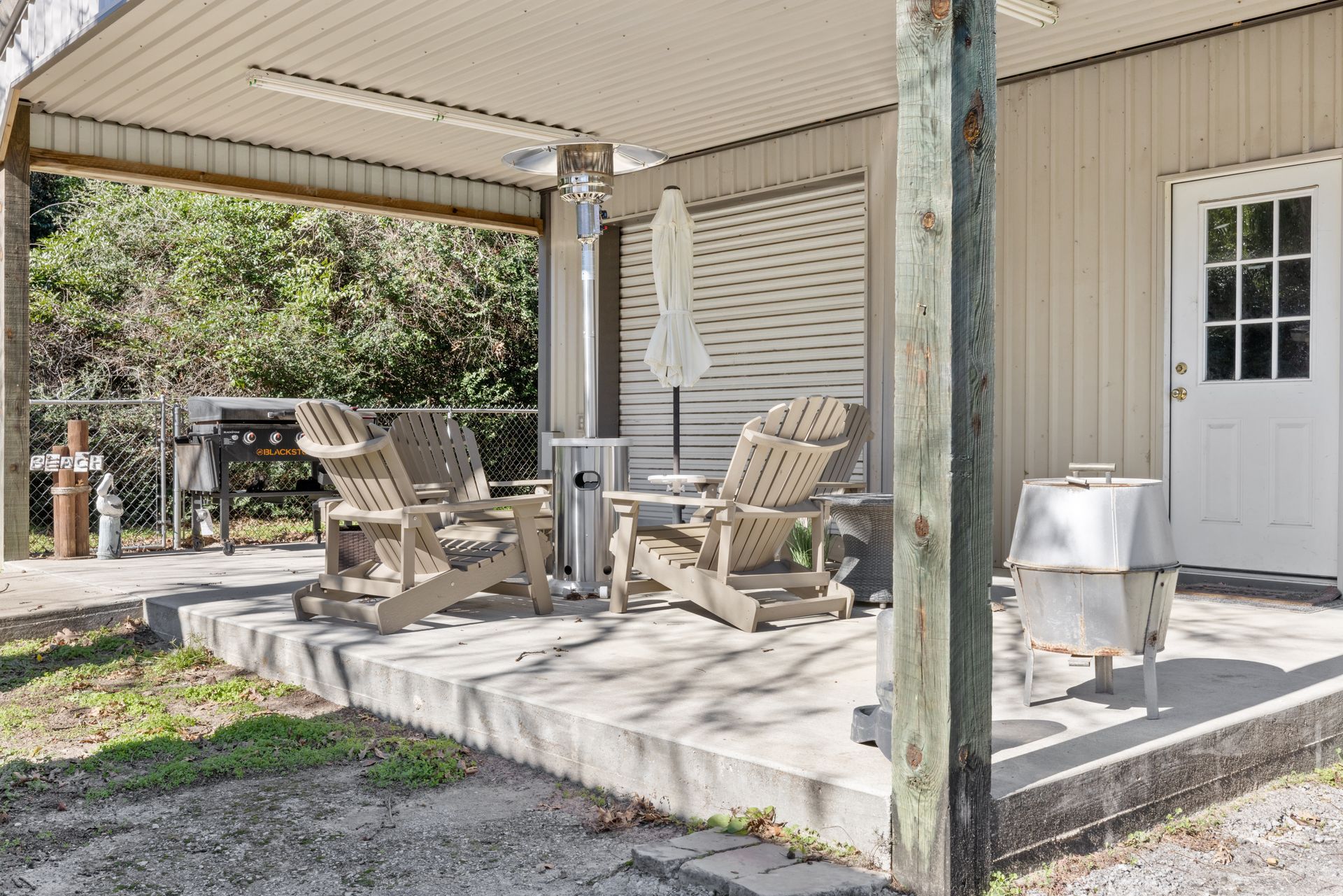 Covered patio with wooden chairs, small table, and grill beside a house door