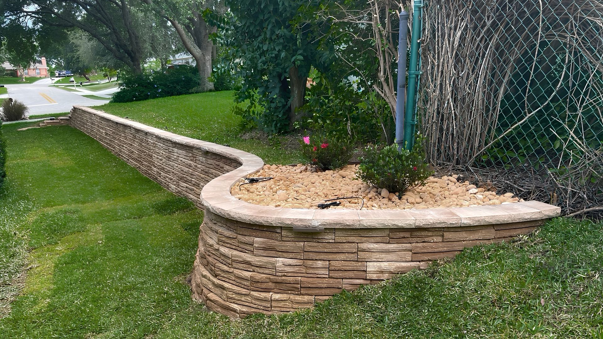 Curved stone retaining wall with mulch beds and trees along a grassy yard