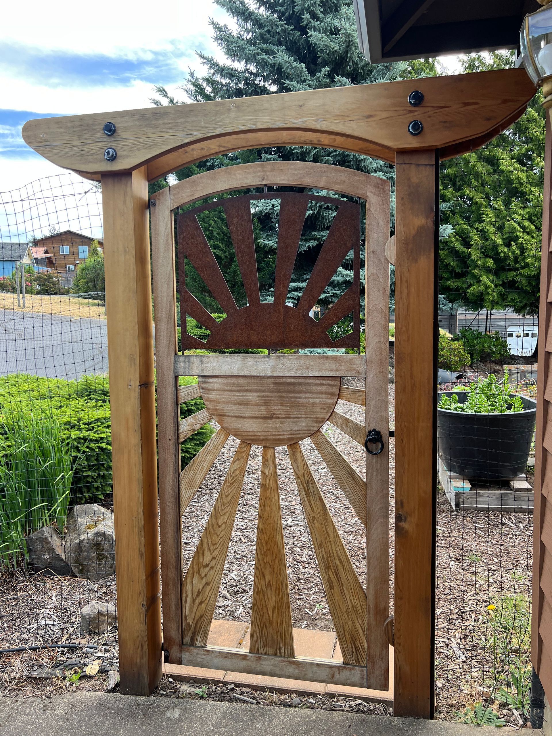 A wooden gate with a sun on it is in a garden.