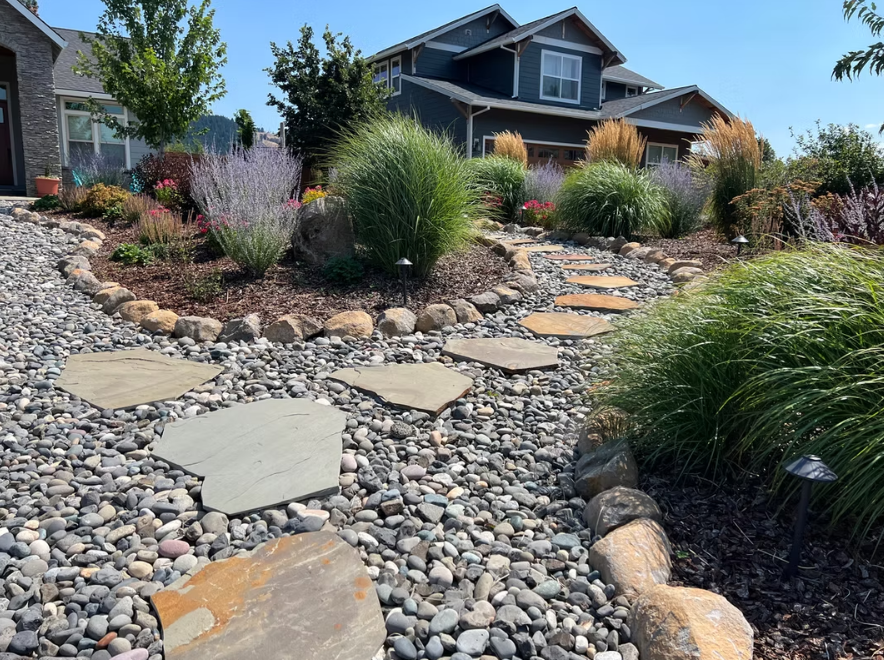 A stone walkway leading to a house surrounded by rocks and plants.