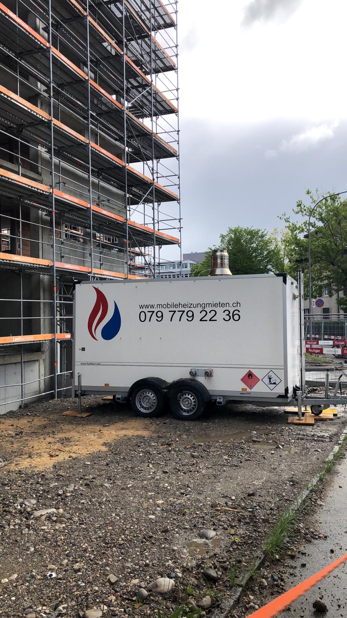 Ein weißer Anhänger steht vor einem im Bau befindlichen Gebäude.