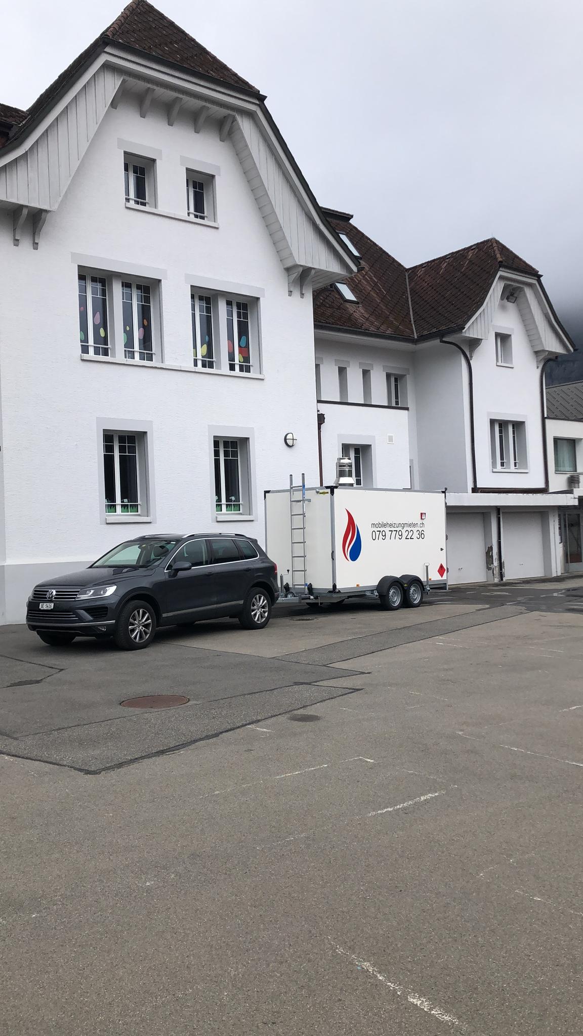 Vor einem weißen Gebäude parkt ein Auto mit einem daran befestigten Anhänger.