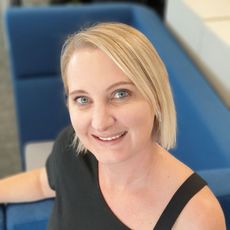 Zelda Kalmeier Smiling seated on a blue couch in a bright office setting