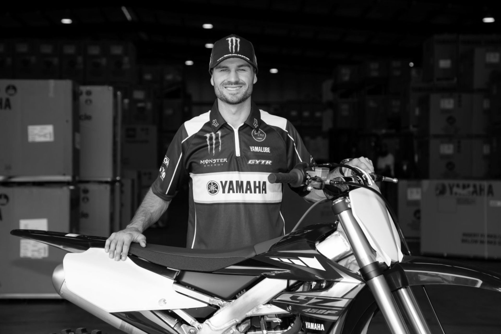 Man in Yamaha jersey with motorcycle, smiling in warehouse setting.