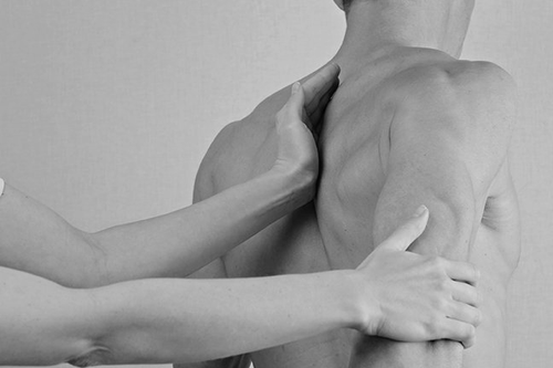 Hands examining a person's shoulder and upper back area, likely for a physical assessment or treatment.