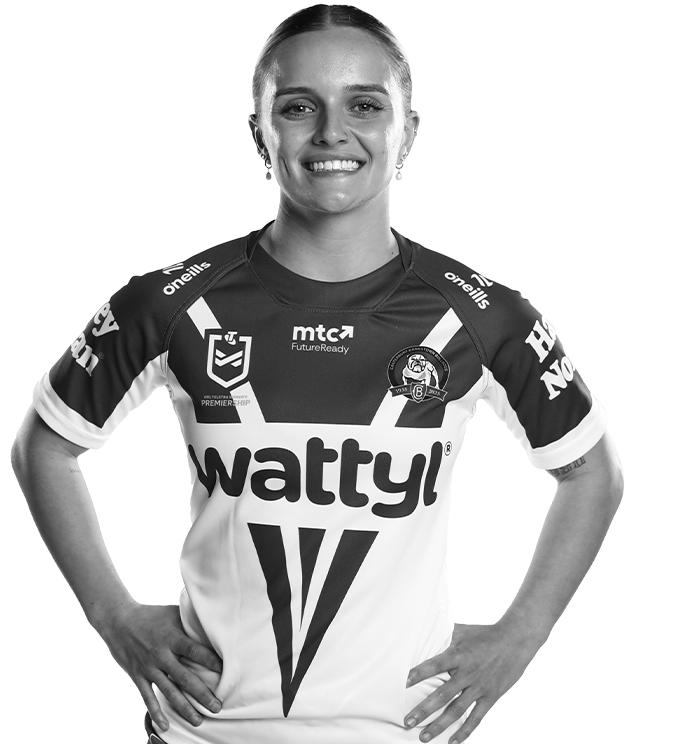 Woman in rugby league jersey, smiling with hands on hips.