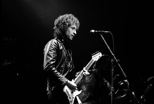 Fotografía en blanco y negro de un guitarrista cantando en un micrófono en el escenario durante un concierto en vivo.