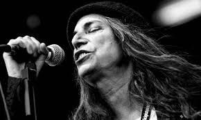 Primer plano en blanco y negro de una cantante inclinándose hacia un micrófono mientras actúa en el escenario.