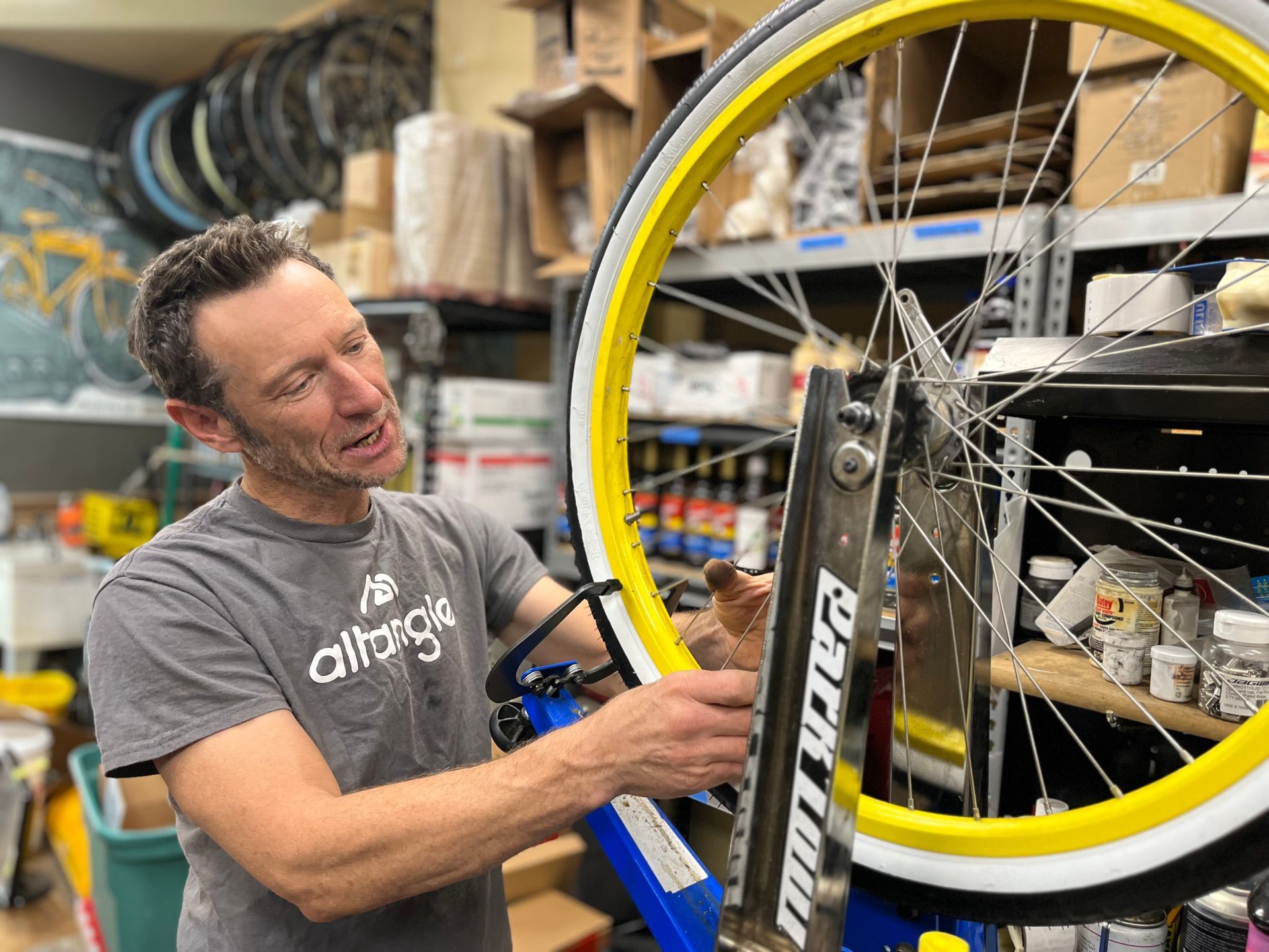 A man is working on a bicycle wheel in a garage.