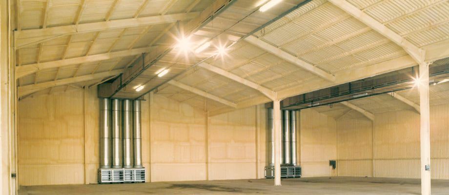 Interior view of a large warehouse with visible ventilation equipment and overhead lighting. The interior is tan in color.