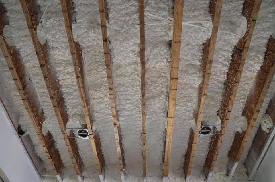 Wooden beams with white spray foam insulation between them, viewed from below.