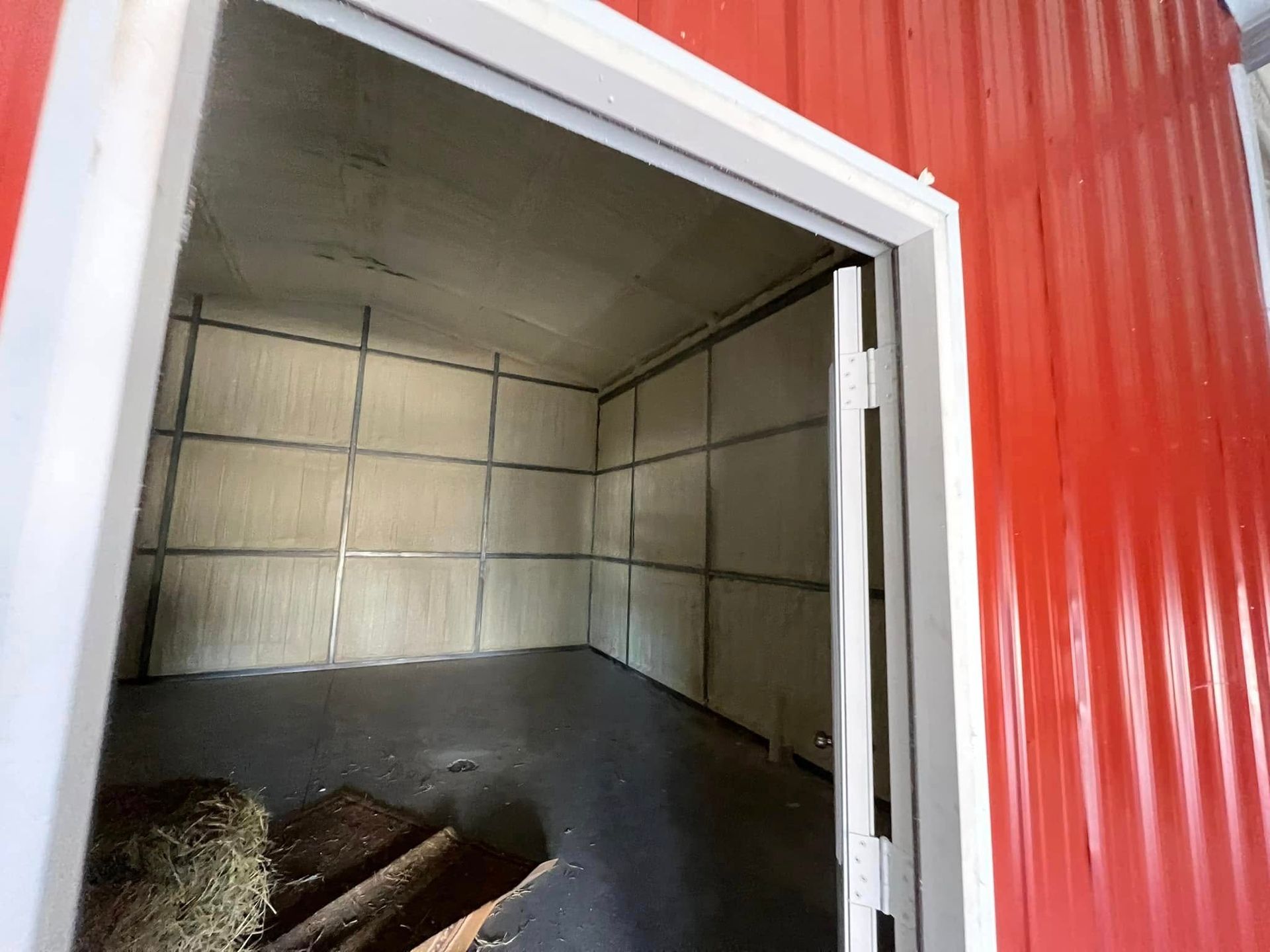 Interior of a red metal building with an open door. The walls and ceiling are insulated.