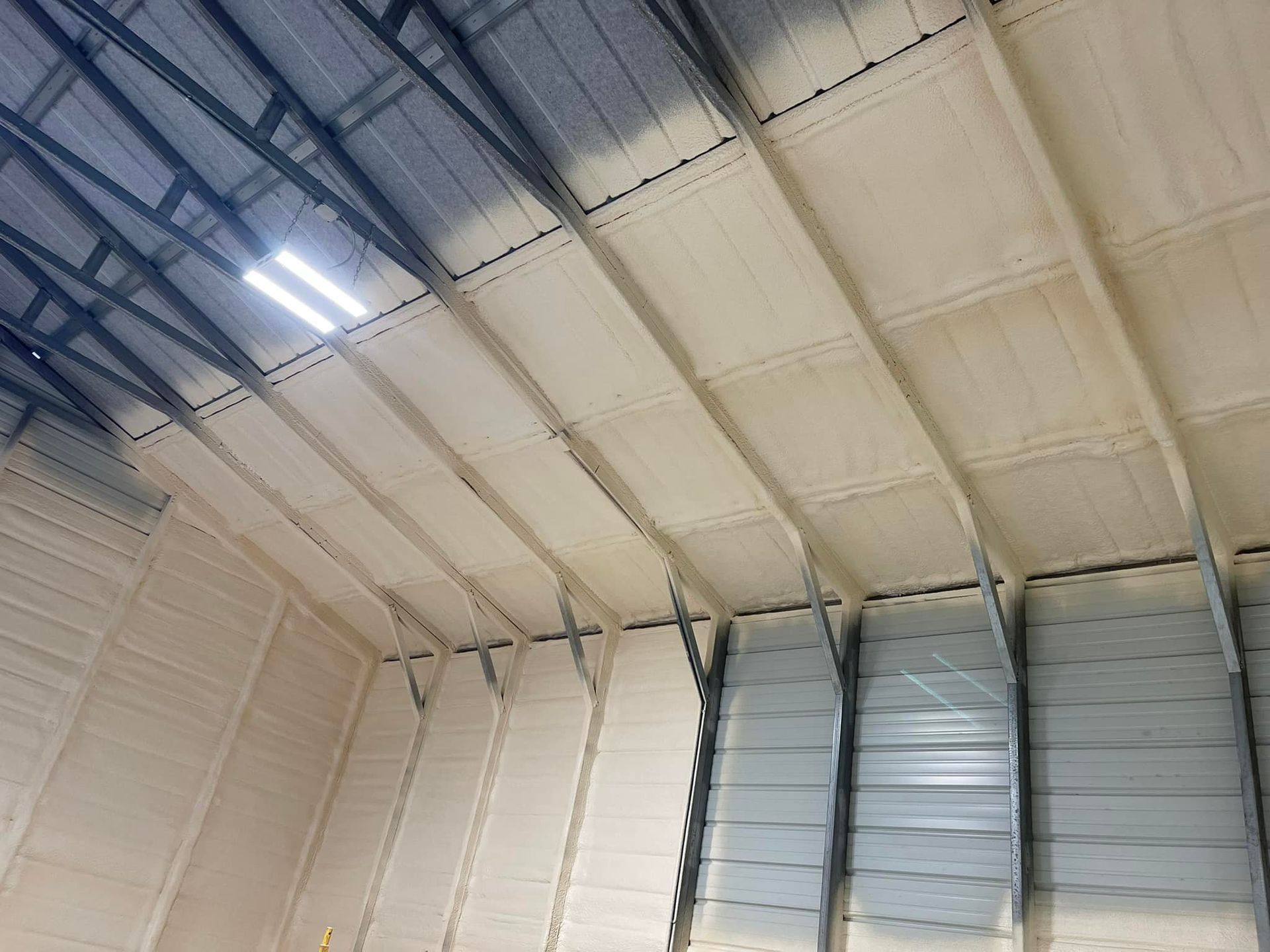 Insulated warehouse ceiling with beige spray foam between metal beams.