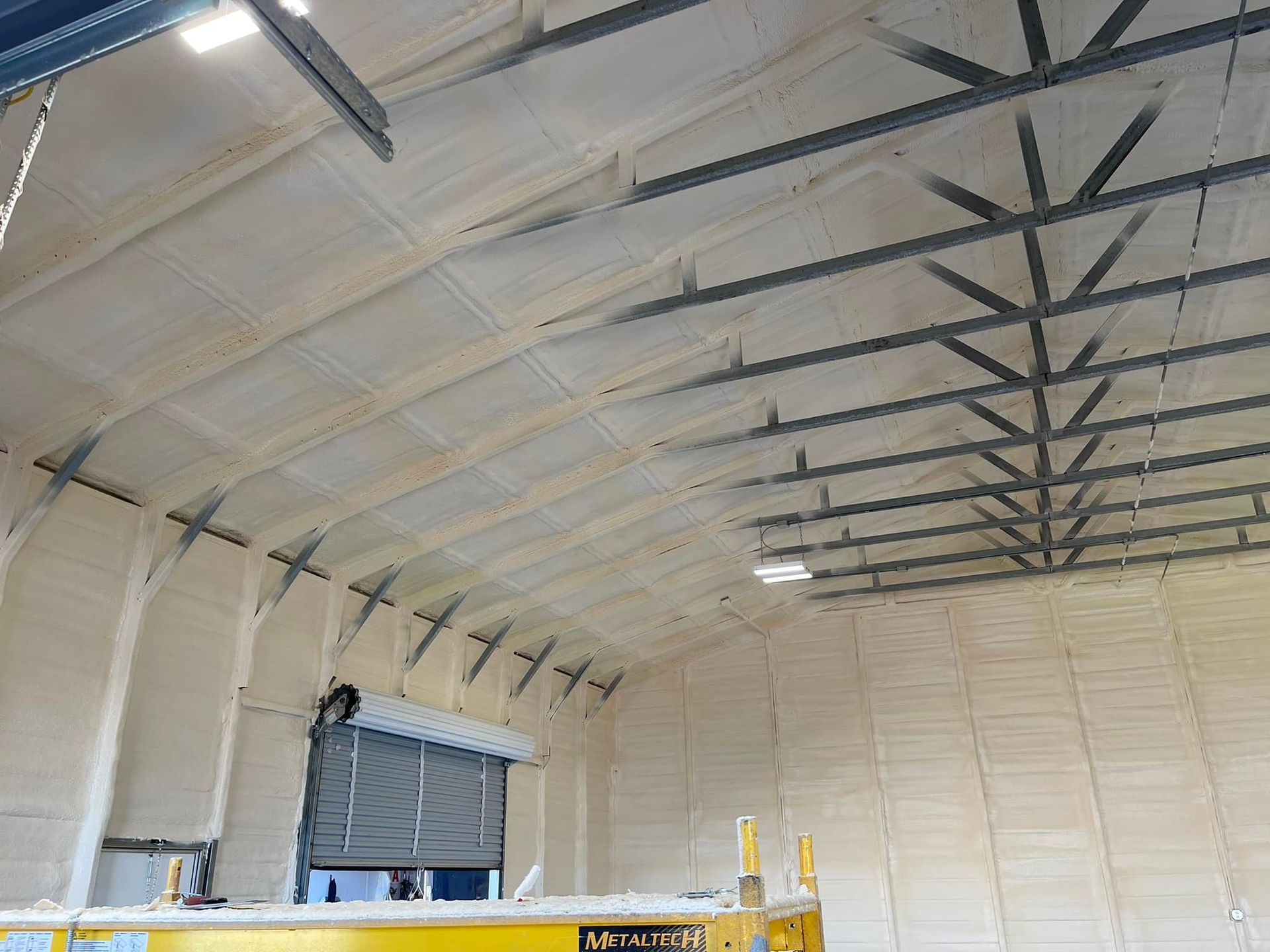 Warehouse interior with spray foam insulation on walls and ceiling, metal beams.