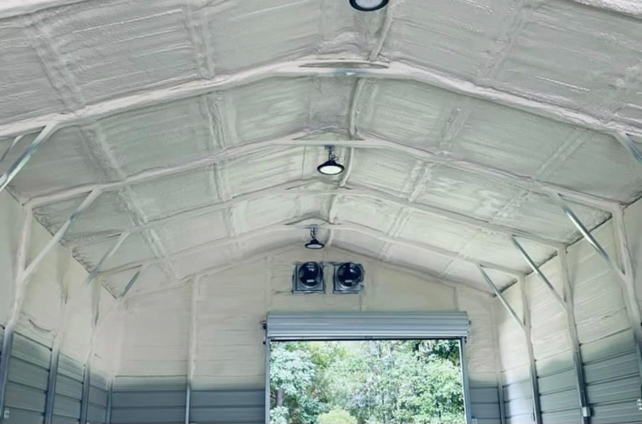 Interior of a metal building insulated with white spray foam. Ceiling lights and ventilation fans are installed.