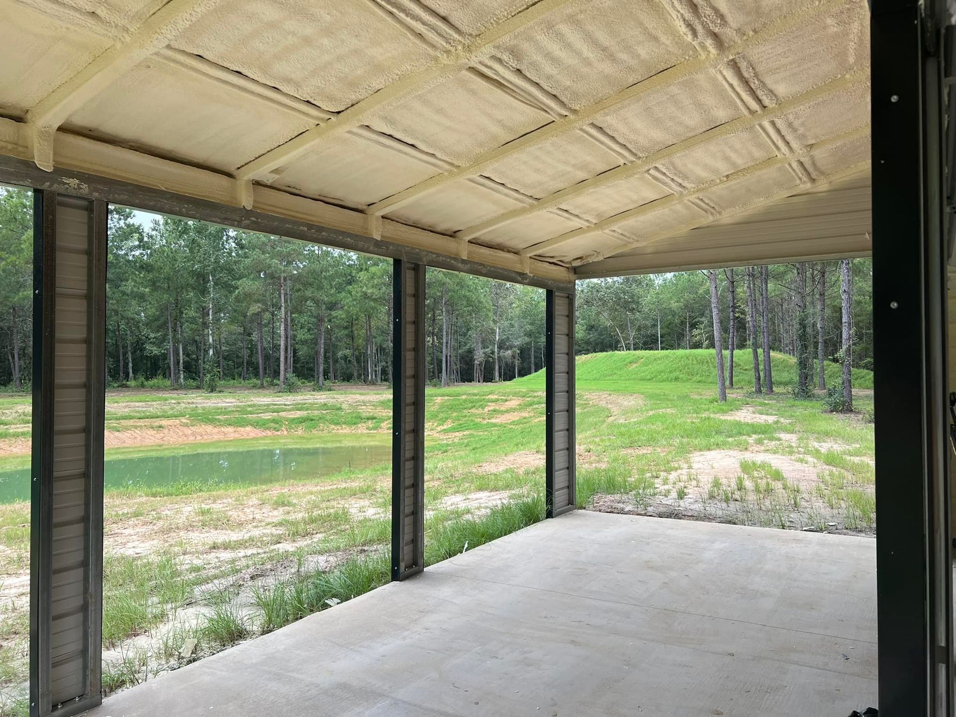 Covered patio with spray foam ceiling, overlooking a pond and trees.