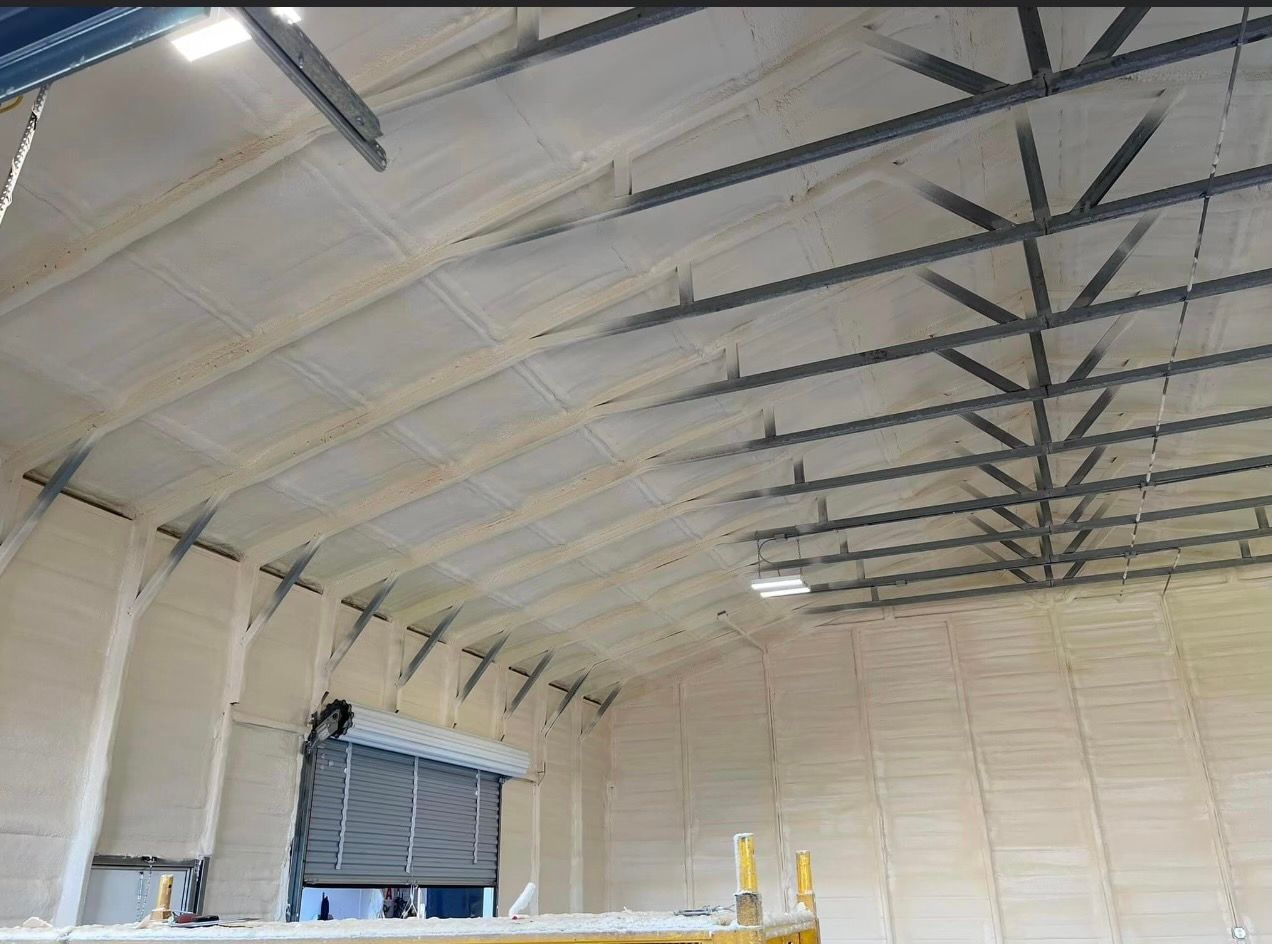 Interior of a building with arched ceiling, insulated with light-colored spray foam; steel trusses are visible.